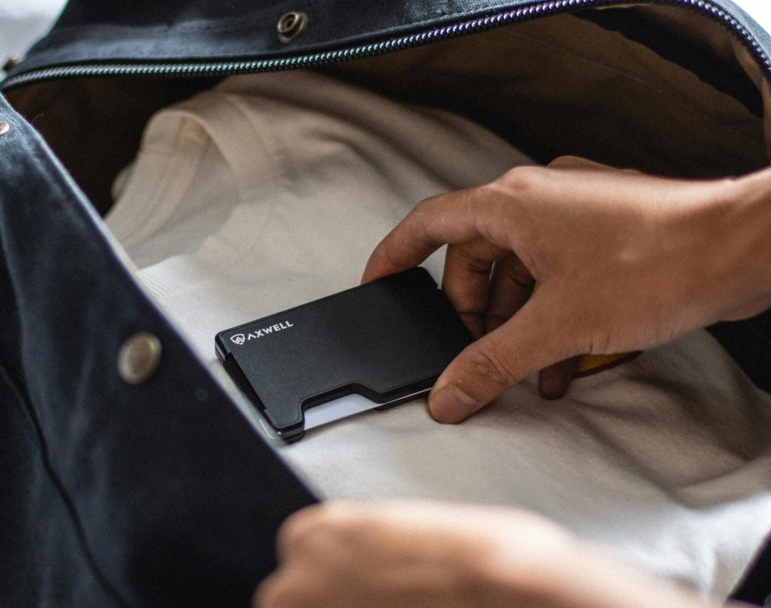 Close-up of a person placing a wallet into a travel bag indoors.