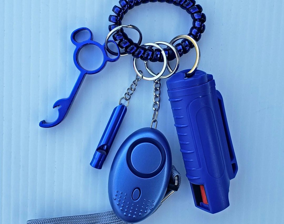 Close-up of blue personal safety items on a keychain, including a whistle and pepper spray.