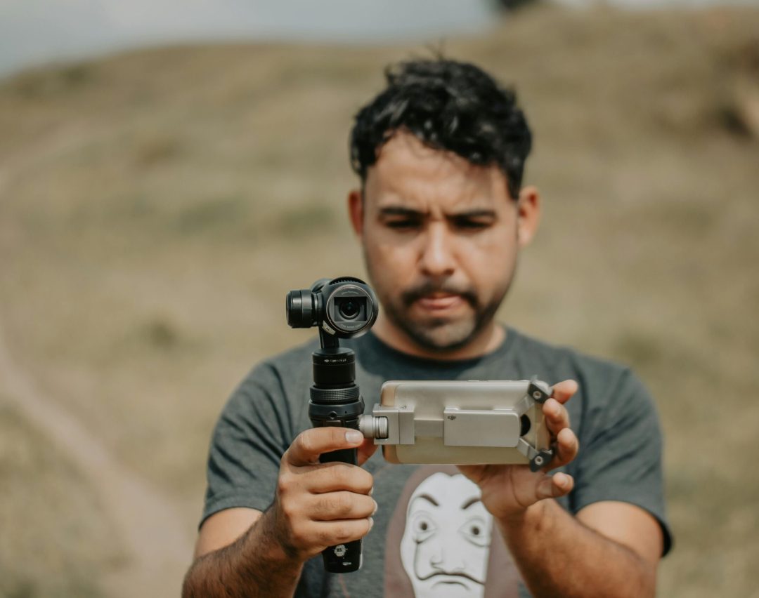 Man using a smartphone gimbal for videography on a grassy field.