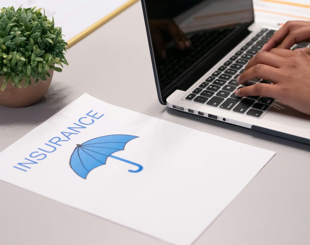 Close-up of hands typing on laptop with an insurance document visible on the desk.
