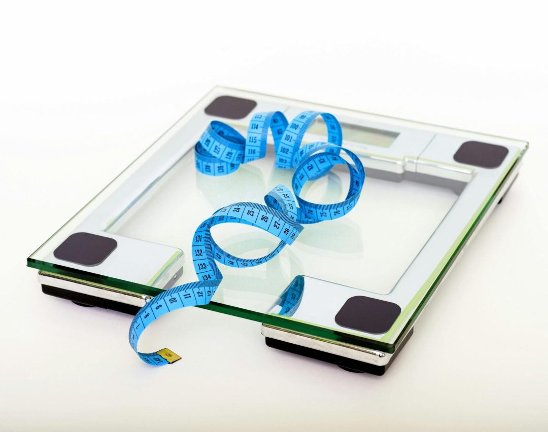 A digital glass weighing scale with a blue measuring tape, symbolizing weight management.